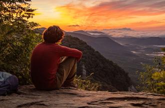 person sitting on rock watching sunset