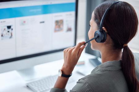 Photo of person taking phone call with a headset and computer